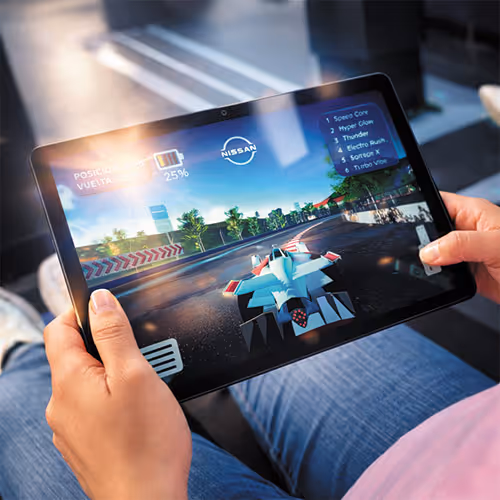 Person holding a tablet displaying a futuristic racing game with a Nissan logo on screen.